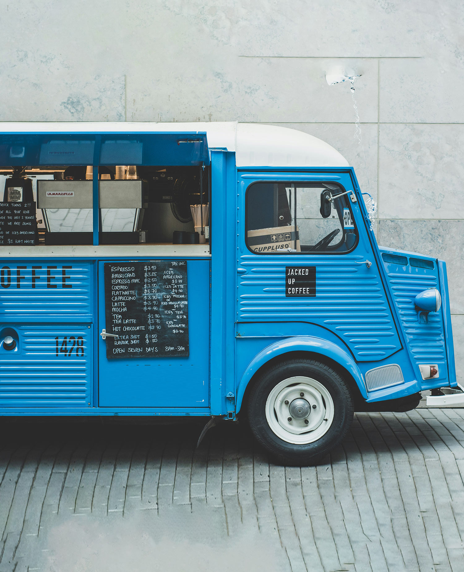 blue food truck selling coffee without any people nearby on a grey cobblestone path
