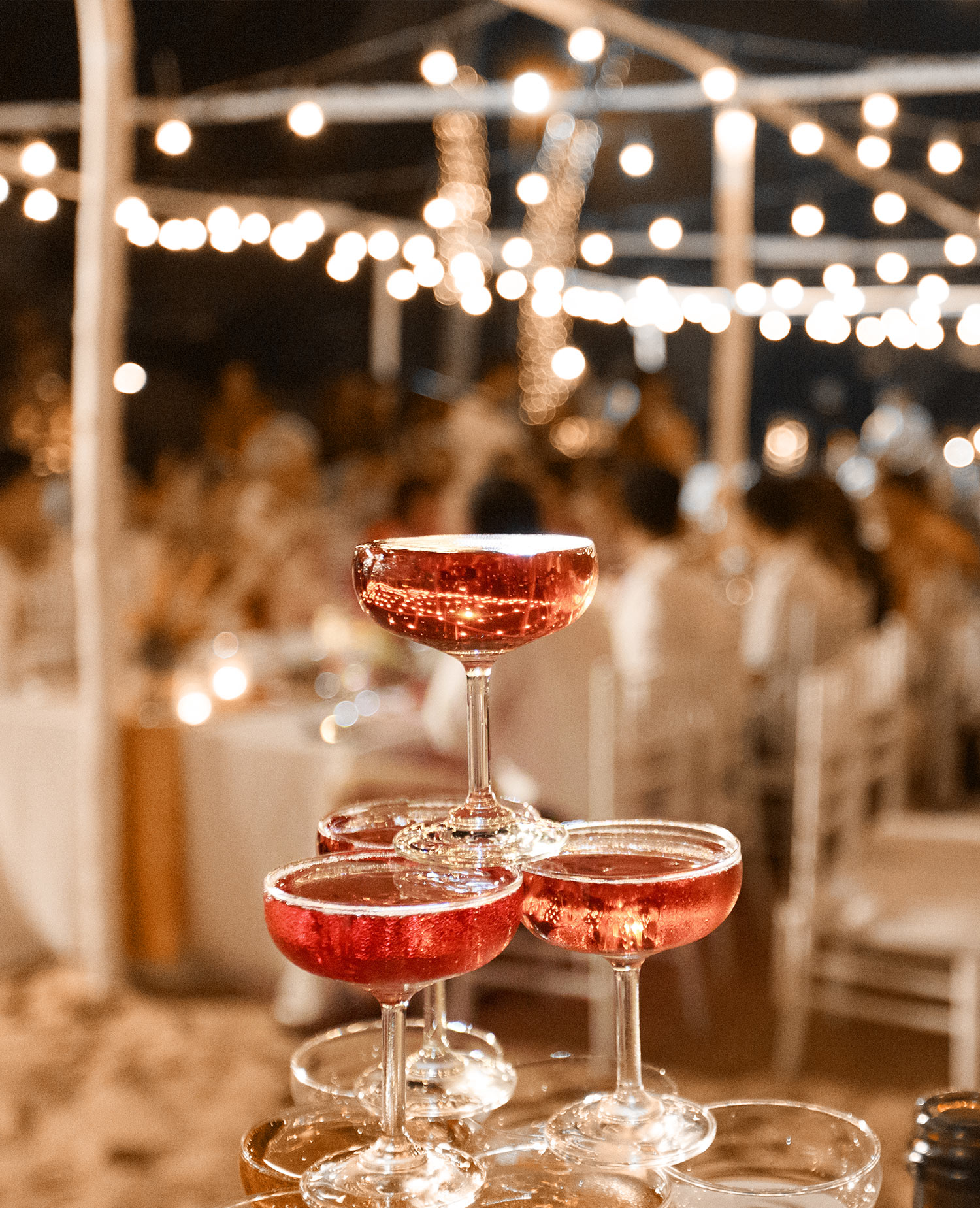 an elegant champagne tower at a party with twinkle lights hanging from the ceiling