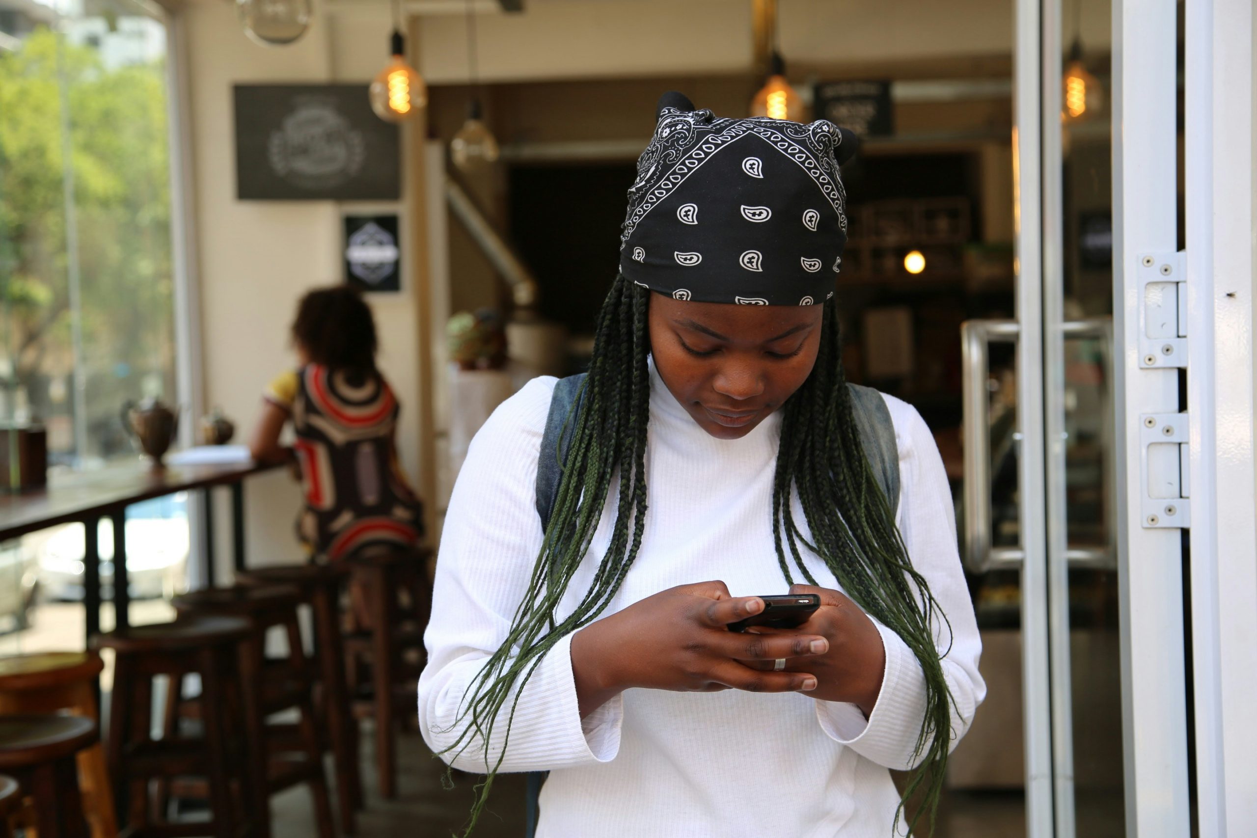 women looking down texting leaving a cafe with a bandana in her hair